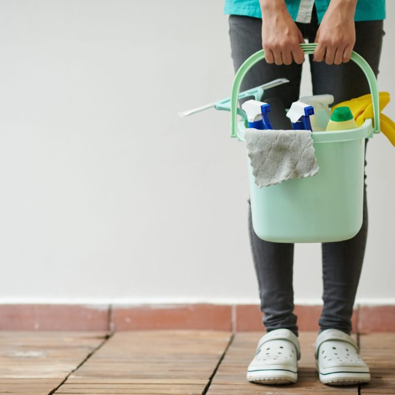 Close-up of cleaning worker holding bucket with different supplies for housework
